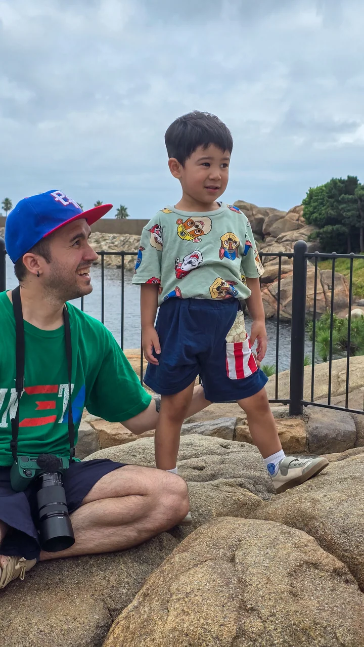 Un padre sonríe hacia su hijo menor, que está de pie orgullosamente sobre unas rocas junto al agua en Tokyo DisneySea.
