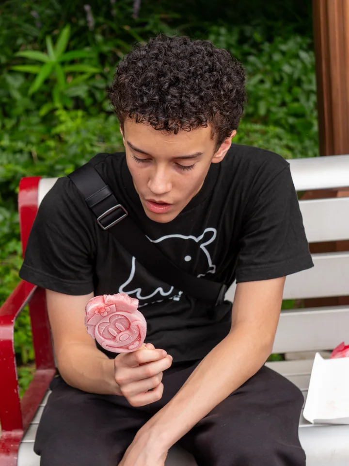 El hijo mayor examina una paleta rosada con forma de Mickey mientras está sentado en un banco.
